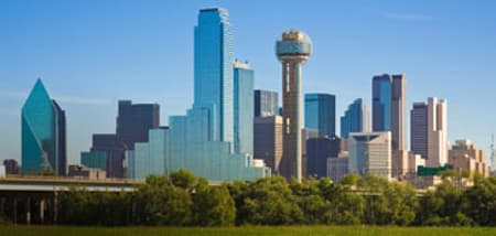 The Dallas skyline features modern skyscrapers and the Reunion Tower under a clear blue sky.