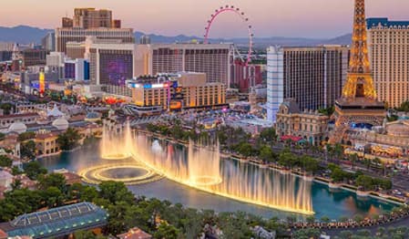 The illuminated Las Vegas Strip at sunset with dancing fountains and prominent hotels.