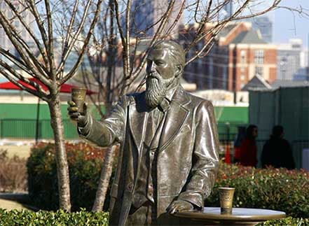 Bronze statue of a bearded man in a suit raising a cup.