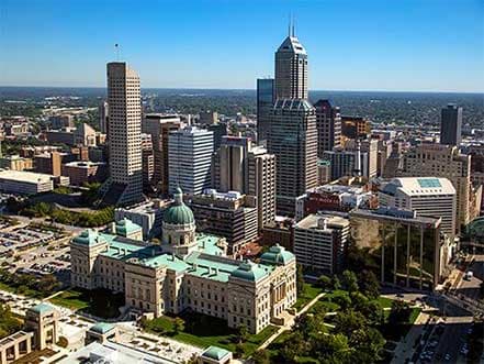 Aerial view of Indianapolis skyline featuring the Statehouse with a green dome and skyscrapers.