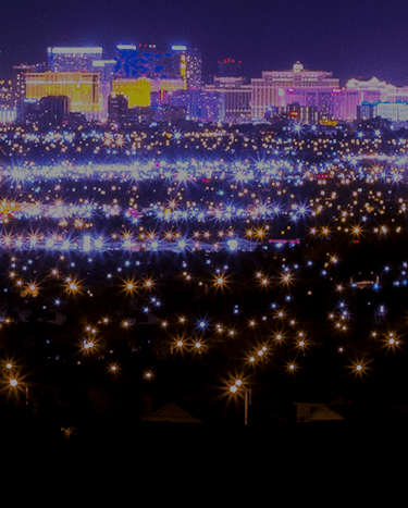 Nighttime aerial view of a vibrant city skyline with numerous sparkling lights in the foreground.
