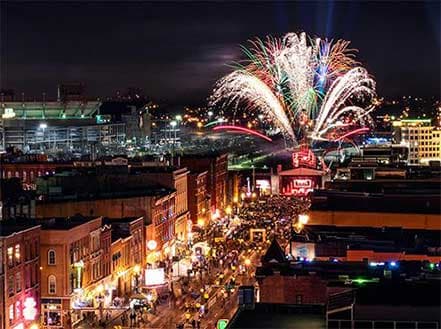 Vibrant fireworks illuminate a bustling Nashville street filled with a large crowd at night.